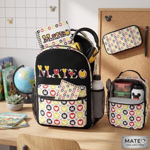 Op de afbeelding: Zwarte rugzak, lunchtas en etui set met een Mickey Mouse-thema patroon van harten en Mickey Mouse-hoofden. De rugzak heeft de naam "MATEO" in kleurrijke letters. Inclusief een waterfles en koptelefoon.