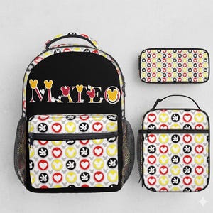 Op de afbeelding: Een zwarte rugzak, etui en lunchtas set. De rugzak heeft de naam "MATEO" in kleurrijke letters. Alle items hebben een patroon van Mickey Mouse-hoofden, harten en handschoenen in rood, geel, zwart en grijs.