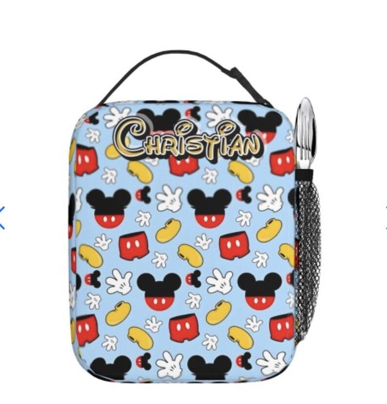 May include: A light blue lunch bag featuring a pattern of Mickey Mouse heads, gloves, shorts, and yellow beans. The name "CHRISTIAN" is written in gold script. A black handle and a mesh pocket with silverware are attached.