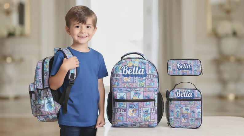 May include: A child stands with a backpack, lunch bag, and pencil case set. The set features a repeating cartoon character pattern in blue, purple, and pink. The name "Bella" is printed on each item. The backpack is designed for school use.