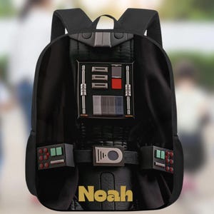 Könnte beinhalten: Schwarzer Rucksack mit Darth-Vader-Design, mit detaillierten Paneelen und einer Gürtelschnalle. Er hat einen oberen Griff und verstellbare Schultergurte. Der Name "Noah" ist unten in Gold aufgedruckt.