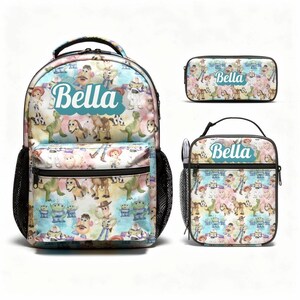 Puede incluir: Una mochila, un estuche rectangular y una bolsa de almuerzo con un patr&oacute;n repetitivo de personajes de Toy Story sobre un fondo de acuarela pastel. Cada art&iacute;culo muestra el nombre Bella en letra blanca sobre un fondo azul verdoso en forma de nube.