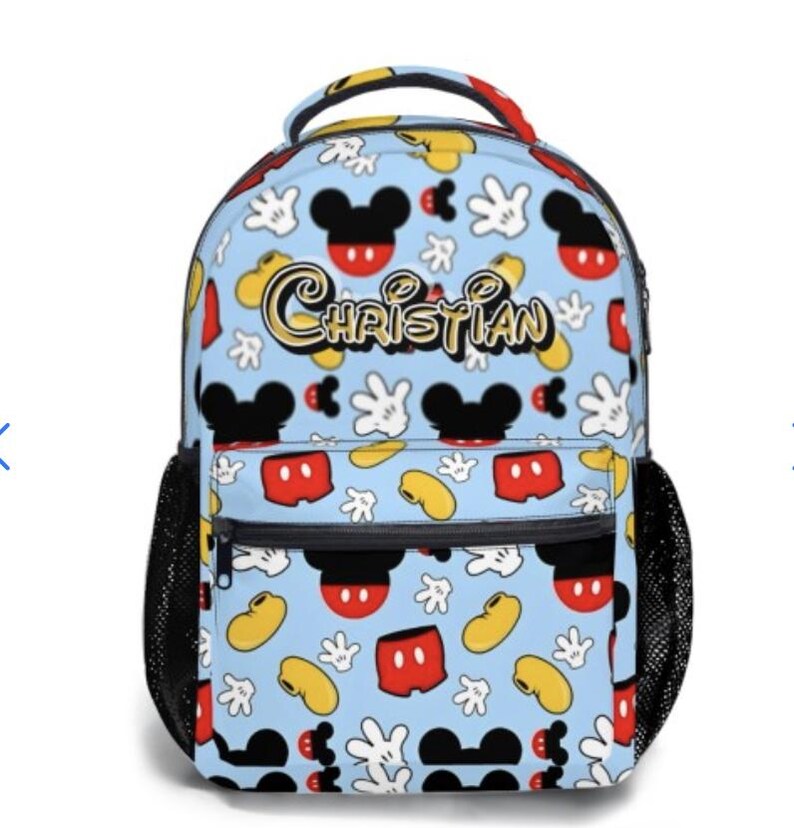 May include: A light blue backpack featuring a pattern of Mickey Mouse heads, gloves, and shorts. The name "CHRISTIAN" is printed in gold script across the front. The backpack has black mesh side pockets and a black zipper.