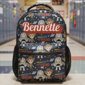 May include: A dark blue backpack featuring a repeating pattern of cartoon characters, stars, and planets. The text "You've got a friend in me" is printed repeatedly, and the name "Bennette" is displayed in large white letters on a red background.