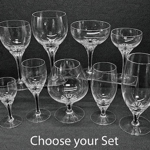 Puede incluir: Una colección de nueve copas de cristal transparente de diversas formas y tamaños, incluyendo copas de vino, de champán y de coñac, todas con un patrón de estrella facetada en la base del cáliz. El texto Choose your Set es visible.
