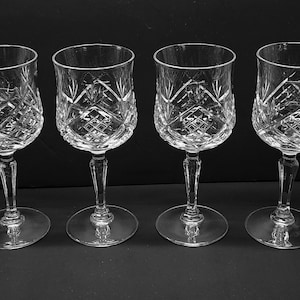 May include: A set of four clear glass wine glasses featuring a detailed diamond and cross-hatch cut pattern on the bowl. Each glass has a slender, faceted stem and a circular base, reflecting light through the intricate geometric glass carvings.