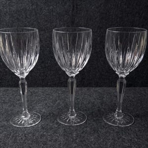 May include: Three clear crystal wine glasses featuring vertical cut patterns on the bowls and faceted stems. Each glass has a circular base with a radiating starburst design, showcasing a transparent finish and a refined, structured silhouette.