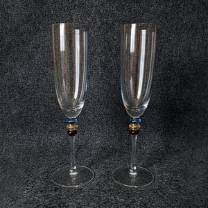 Peut inclure: Deux flûtes à champagne transparentes avec des tiges décoratives. Les tiges présentent des accents bleus, dorés et rouges. Les flûtes sont en verre et ont un design classique et élégant, parfait pour les célébrations.