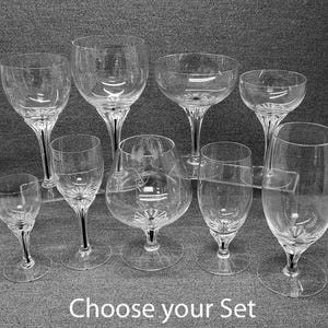 May include: A collection of nine clear glass stemware pieces of varying shapes and sizes, including wine glasses, a brandy snifter, and a tall tumbler, all featuring a faceted base design. The text "Choose your Set" is printed at the bottom.