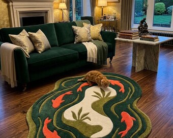 May include: An irregular, organic-shaped area rug featuring a deep green background with concentric wavy lines in lighter green and cream. The rug displays five orange koi fish motifs and a central cream-coloured island with green plant silhouettes.