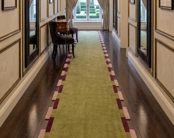 May include: A long hallway featuring a green runner rug with a geometric border of dark red and light pink rectangles. The walls are panelled with gold trim, two tall mirrors, and framed artwork. A dark wood console table and chairs sit nearby.