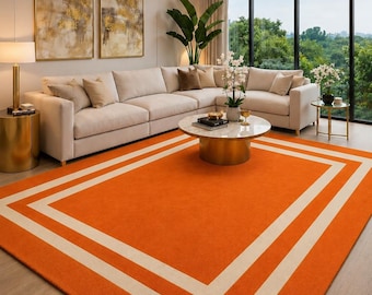 May include: A rectangular area rug featuring a vibrant orange centre field framed by two concentric white rectangular borders. The rug is constructed with a short, dense pile texture and is positioned on a light-toned wooden floor surface.