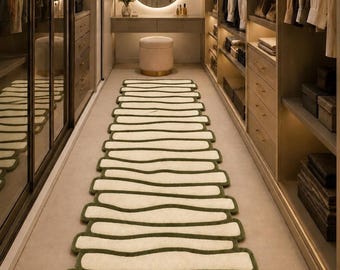 May include: A long runner rug featuring a repeating pattern of cream-coloured, organic, wavy horizontal bars outlined in a deep olive green border. The rug is positioned centrally on the floor, extending lengthwise through the middle of the room.