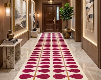 May include: A long rectangular runner rug featuring a cream-coloured background with two symmetrical rows of magenta leaf-shaped patterns connected by thin gold lines, centred in a hallway with marble flooring and wood-panelled walls.