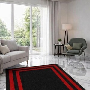 May include: A rectangular area rug featuring a solid black center framed by two bold red stripes and a black border. The rug is positioned on a white marble floor in a living room containing a gray sofa, a gray armchair, and a floor lamp.