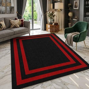May include: A rectangular area rug featuring a solid black center field framed by two distinct, bold red rectangular borders. The rug has a low-pile texture and is positioned flat on a white marble floor, showcasing a clean geometric design.