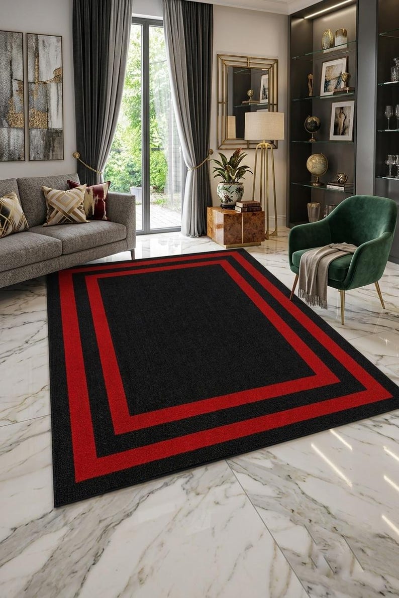 May include: A rectangular area rug featuring a solid black center field framed by two distinct, bold red rectangular borders. The rug has a low-pile texture and is positioned flat on a white marble floor, showcasing a clean geometric design.