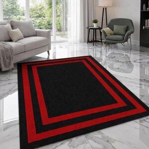 May include: A rectangular area rug featuring a solid black center field framed by two distinct, bold red rectangular borders. The rug has a low-pile texture and is positioned flat on a white marble floor, creating a sharp contrast with the dark colors.