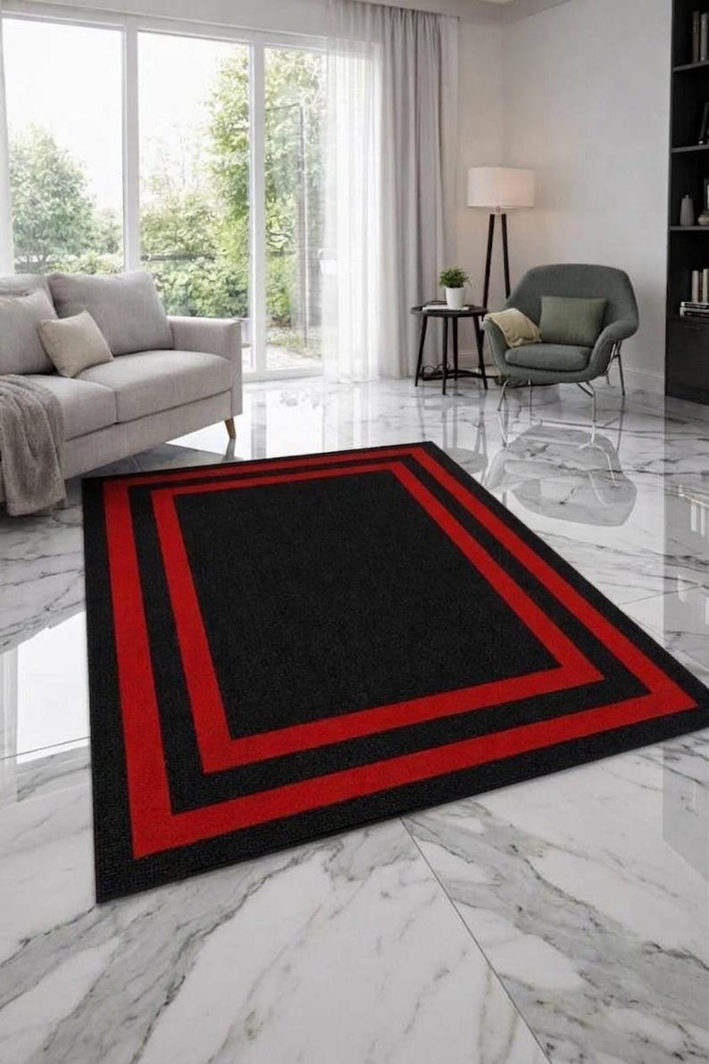 May include: A rectangular area rug featuring a solid black center field framed by two distinct, bold red rectangular borders. The rug has a low-pile texture and is positioned flat on a white marble floor, creating a sharp contrast with the dark colors.