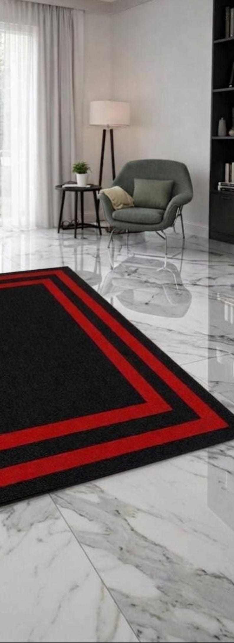 May include: A rectangular area rug featuring a solid black center bordered by two distinct, parallel red stripes that frame the perimeter. The rug is positioned on a white marble floor with grey veining, set within a room containing a grey armchair.