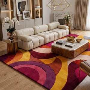 May include: A large area rug featuring a bold, geometric pattern of concentric semicircles in vibrant shades of magenta, deep purple, orange, and yellow. The rug has a plush, textured pile and covers a significant portion of the wooden floor.