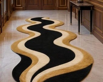 May include: A long, runner-style rug featuring a wavy, organic shape. The design consists of alternating, flowing bands of solid black, cream, and golden-brown colours that create a continuous, undulating pattern across the entire surface.