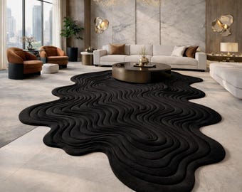May include: A large, black area rug with an irregular, organic shape and a textured, wavy, rippled pattern that mimics flowing liquid. The rug is positioned on a light-coloured floor in a room with a sofa, armchairs, and a coffee table.