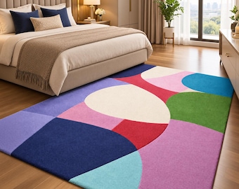 May include: A rectangular area rug featuring a bold, abstract pattern of large, overlapping geometric shapes in vibrant colours including navy blue, light blue, purple, pink, red, green, and cream, laid on a wooden floor.