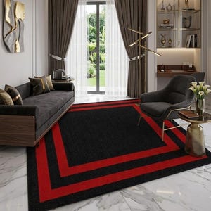 May include: A rectangular area rug featuring a solid black center bordered by two distinct, bold red rectangular frames. The rug is positioned on a white marble floor, providing a sharp contrast between the dark textile and the light stone surface.
