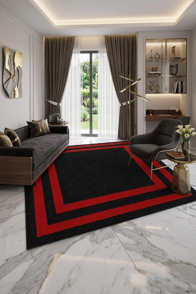May include: A rectangular area rug featuring a solid black center bordered by two distinct, bold red rectangular frames. The rug is positioned on a white marble floor, providing a sharp contrast between the dark textile and the light stone surface.