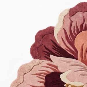 May include: A tufted rug shaped like a large flower, featuring layered petals in shades of deep burgundy, dusty rose, soft pink, and cream. The textured surface displays varying pile heights to create depth and definition within the floral design.