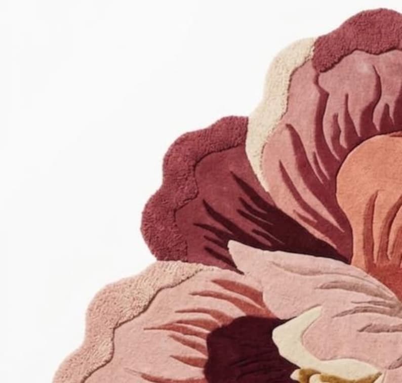 May include: A tufted rug shaped like a large flower, featuring layered petals in shades of deep burgundy, dusty rose, soft pink, and cream. The textured surface displays varying pile heights to create depth and definition within the floral design.
