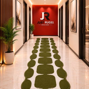 May include: A long runner rug featuring a white base with a repeating pattern of dark olive green rounded squares and circles along the edges. The rug is positioned on a polished light-colored floor in a hallway with a red wall and logo at the end.