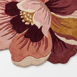 May include: A tufted area rug shaped like a large blooming flower with scalloped edges. The design features layered petals in shades of deep burgundy, dusty rose, soft pink, mustard yellow, and cream, creating a textured floral pattern.