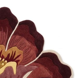 May include: A tufted rug shaped like a large flower with layered petals in shades of deep burgundy, maroon, and muted mauve. The center features golden yellow and light cream accents, with a distinct cream-colored border outlining the petal edges.