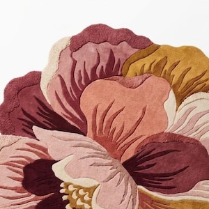 May include: A tufted rug shaped like a large blooming flower with layered petals in shades of deep burgundy, dusty rose, soft pink, cream, and mustard yellow. The rug features a textured surface with scalloped edges and intricate petal detailing.