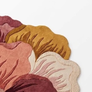 May include: A tufted area rug featuring a large, stylized floral pattern with organic, curved edges. The design incorporates a warm color palette of deep burgundy, muted rose, soft cream, and golden mustard yellow with textured pile details.