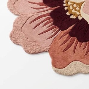 May include: A tufted rug shaped like a large flower with scalloped edges. The design features layered petals in shades of dusty pink, terracotta, and deep burgundy, with a central cluster of cream and mustard yellow tufted textures.