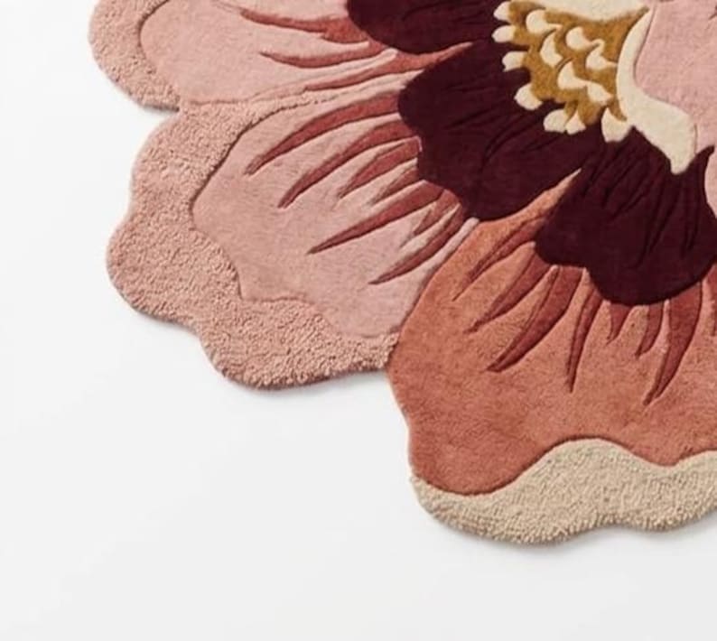 May include: A tufted rug shaped like a large flower with scalloped edges. The design features layered petals in shades of dusty pink, terracotta, and deep burgundy, with a central cluster of cream and mustard yellow tufted textures.
