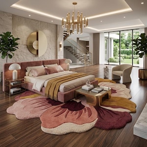 May include: A large, flower-shaped area rug featuring layered petals in shades of dusty pink, deep burgundy, and mustard yellow. The rug is placed on a dark wood floor beneath a pink upholstered bed frame with a mustard yellow throw blanket.