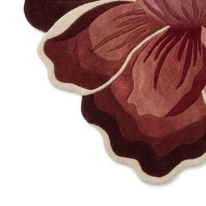May include: A tufted rug shaped like a large flower with layered petals in shades of deep burgundy, dark red, and muted rose. The edges of the petals are outlined with a thick, cream-colored border, creating a distinct contrast against the dark tones.