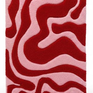 May include: A rectangular rug with a wavy pattern in shades of red and light pink. The design features flowing, organic shapes that create a visually appealing contrast. The rug has a soft, textured appearance.