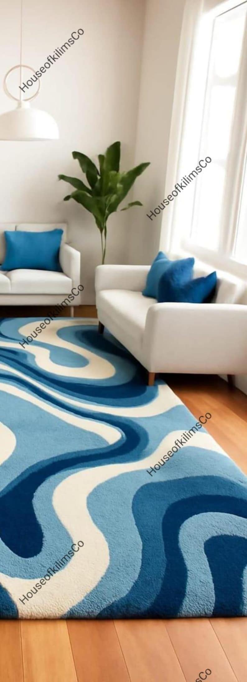 May include: A blue and white patterned rug with a wavy design, placed in a living room setting. The rug is the focal point, complemented by white sofas, blue cushions, and a green plant. The room has hardwood floors.