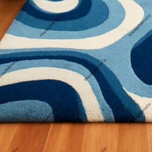 May include: A blue and white patterned rug with a retro design. The rug features a series of curved lines in shades of blue and white, creating a wave-like pattern. The rug is made of a soft, textured material.