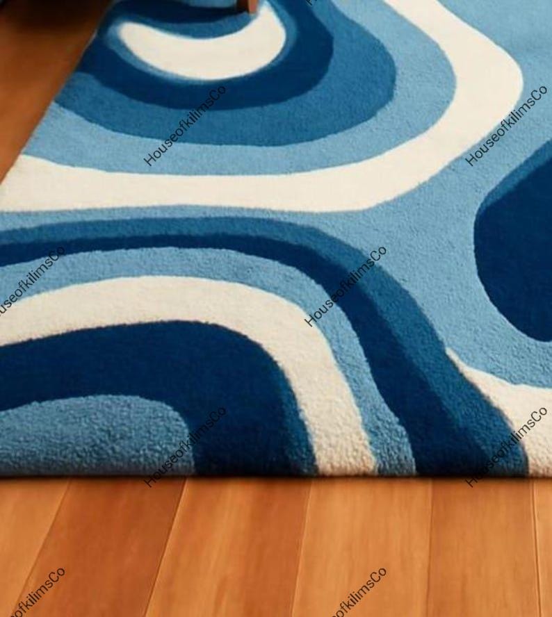 May include: A blue and white patterned rug with a retro design. The rug features a series of curved lines in shades of blue and white, creating a wave-like pattern. The rug is made of a soft, textured material.