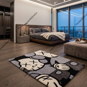 May include: A modern bedroom featuring a large bed with gray bedding and a plush throw. A gray and black cartoon character rug is on the wooden floor. A cat rests on a matching ottoman near a large window with a city view.