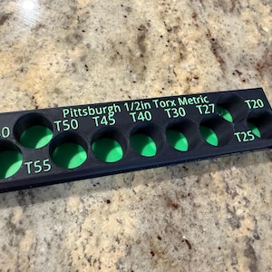 Könnte beinhalten: Ein schwarzer, 3D-gedruckter Werkzeughalter mit grünen Innenräumen, beschriftet mit "Pittsburgh 1/2in Torx Metric". Er verfügt über kreisförmige Schlitze mit den Größen T20 bis T60, die zum Organisieren und Aufbewahren verschiedener Torx-Bits dienen. Der Werkzeughalter ist für 1/2-Zoll-Torx-Bits konzipiert.