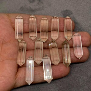 May include: A collection of eleven clear, double-terminated quartz crystal points. Each crystal features a hexagonal, elongated shape with pointed ends on both sides. The stones are transparent, colorless, and have smooth, faceted surfaces.