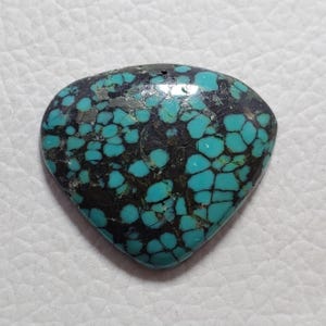 May include: A heart-shaped turquoise gemstone, polished to a high sheen. The stone features a matrix of dark brown and silver, with vibrant blue-green turquoise inclusions. The gemstone is likely intended for use in jewellery or decorative items.