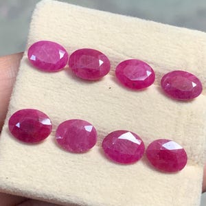 Peut inclure: Huit rubis à facettes de forme ovale disposés en deux rangées de quatre. Chaque pierre précieuse présente une teinte rose-rouge profonde et vibrante avec des inclusions internes visibles et une surface polie reflétant la lumière.